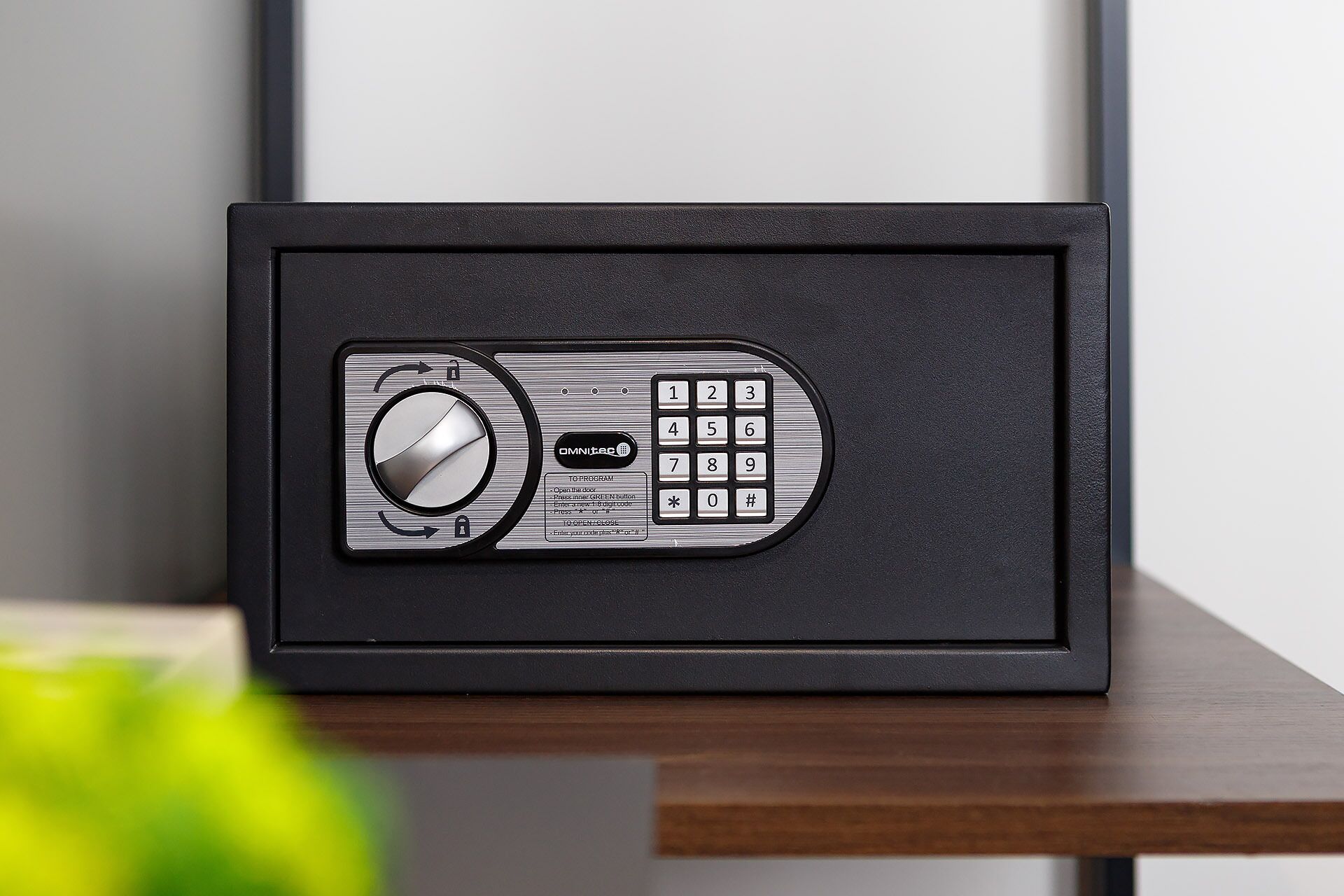 A black safe with a combination dial and keypad, placed on a wooden surface.