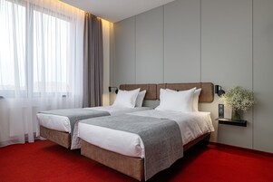 Habitación de hotel con dos camas, alfombra roja, lámpara de pared y un florero con flores.
