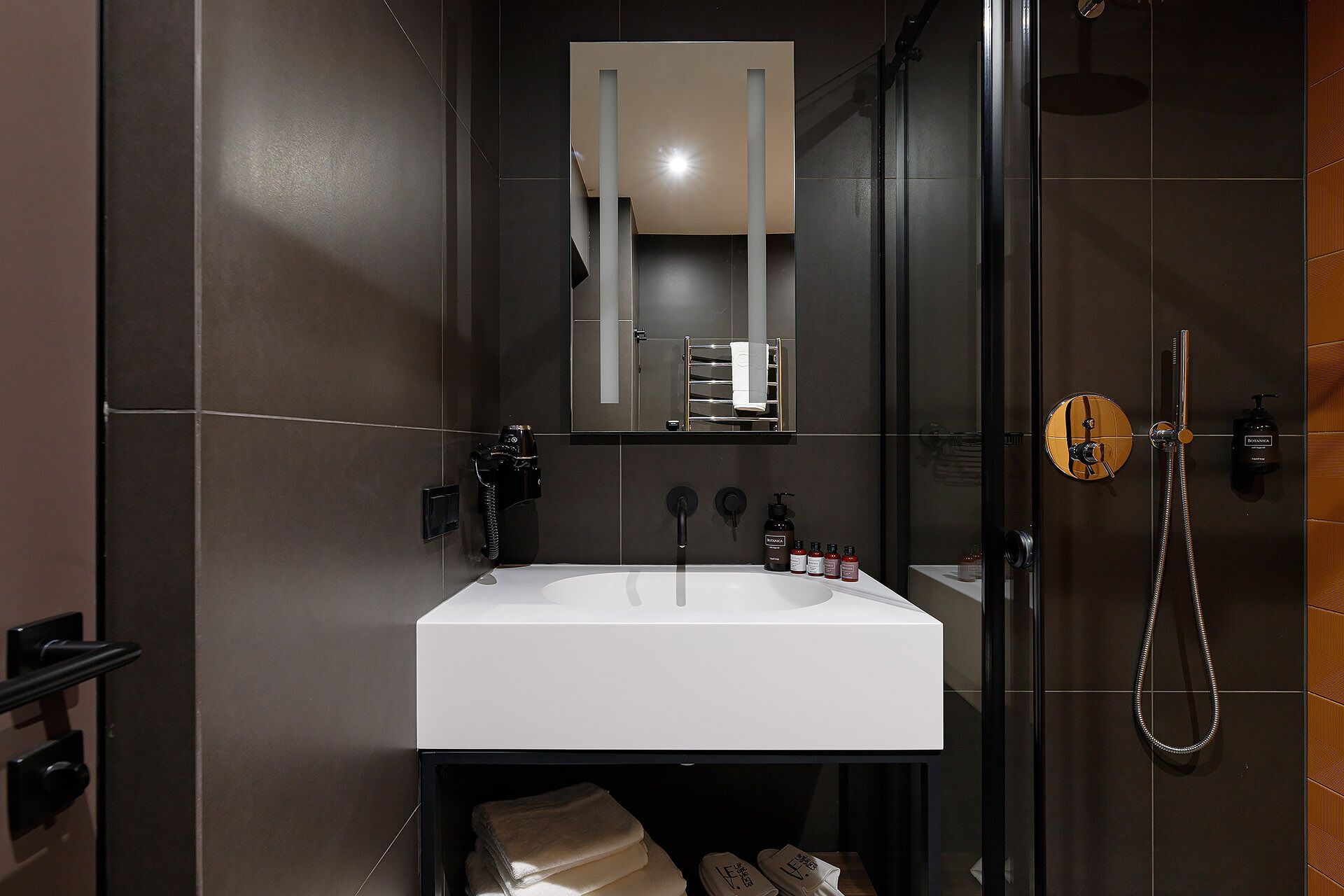 A modern bathroom with a white sink, a glass shower enclosure, and a towel rack.