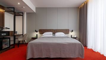 Een hotelkamer met een bed, een bureau met stoel, een kluisje en een rode tapijt.