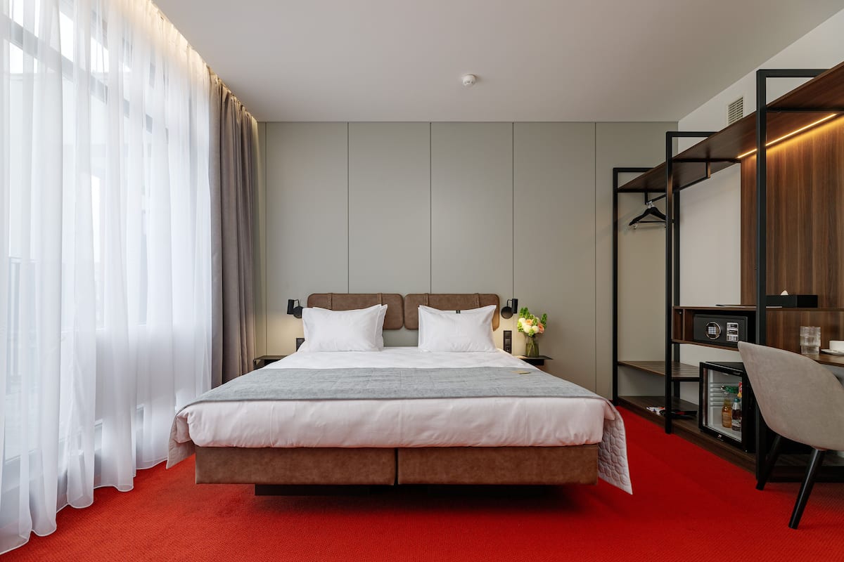 Moderni hotellihuone, jossa on suuri sänky, työpöytä ja vaatekaappi.
