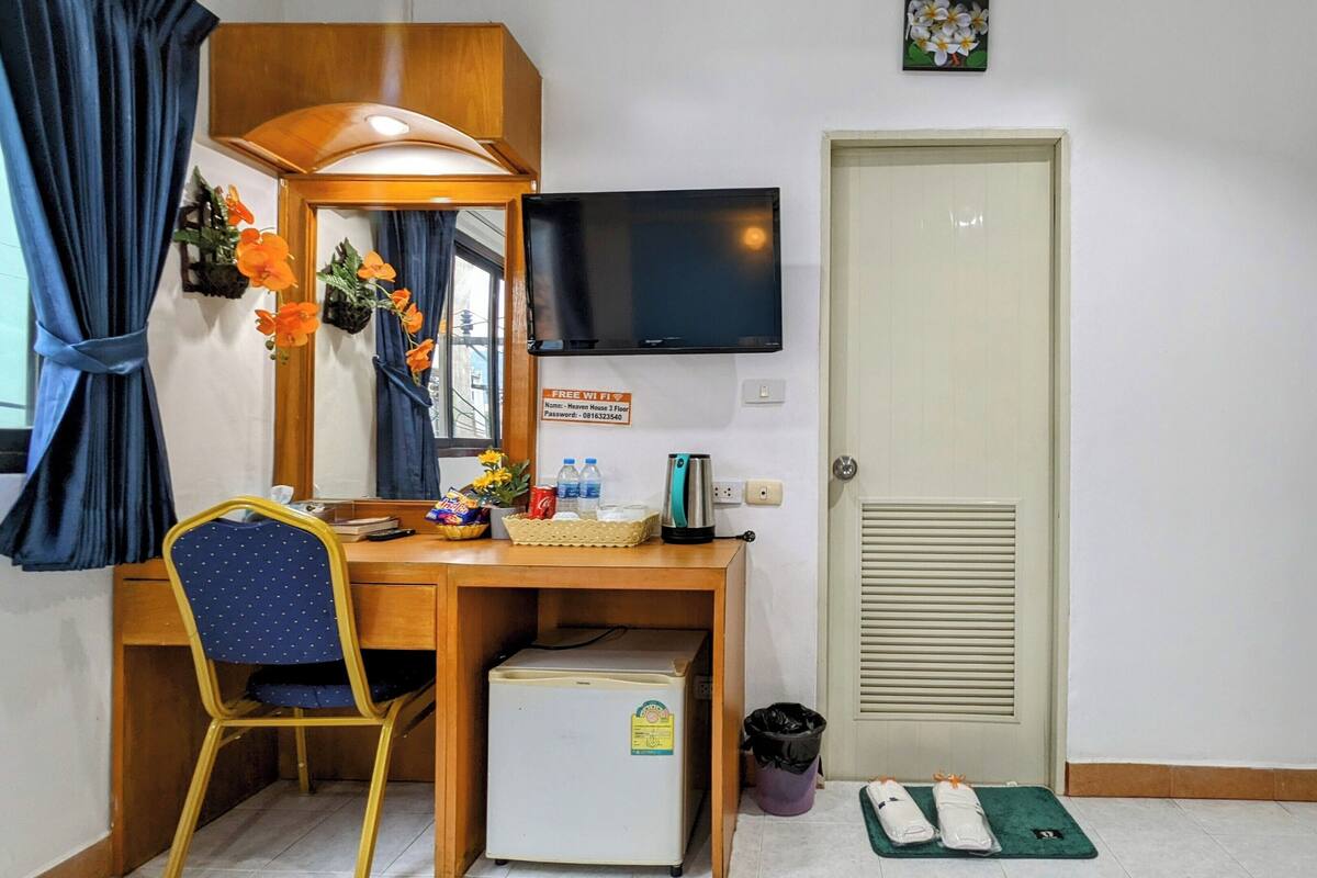 A compact hotel room with a desk, chair, small refrigerator, and a TV.