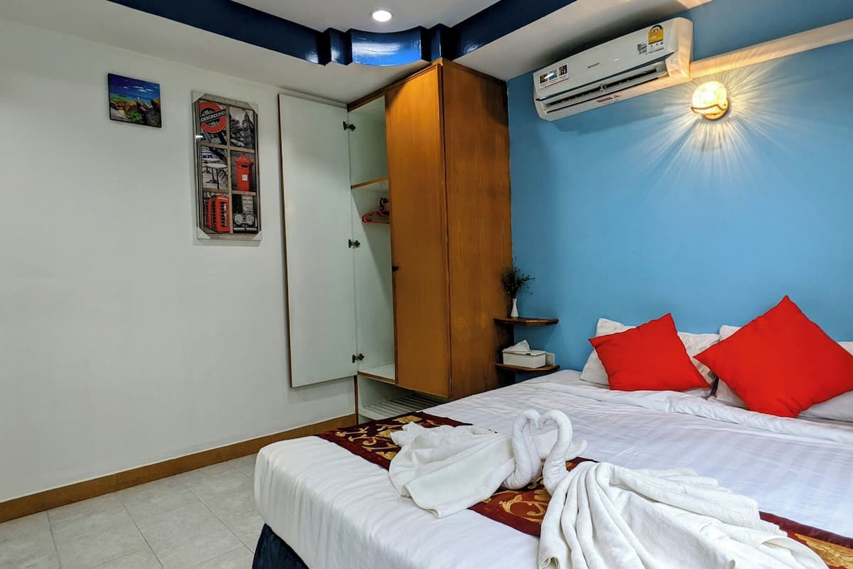 A hotel room with a bed, red pillows, a white blanket, and a towel on the bed.