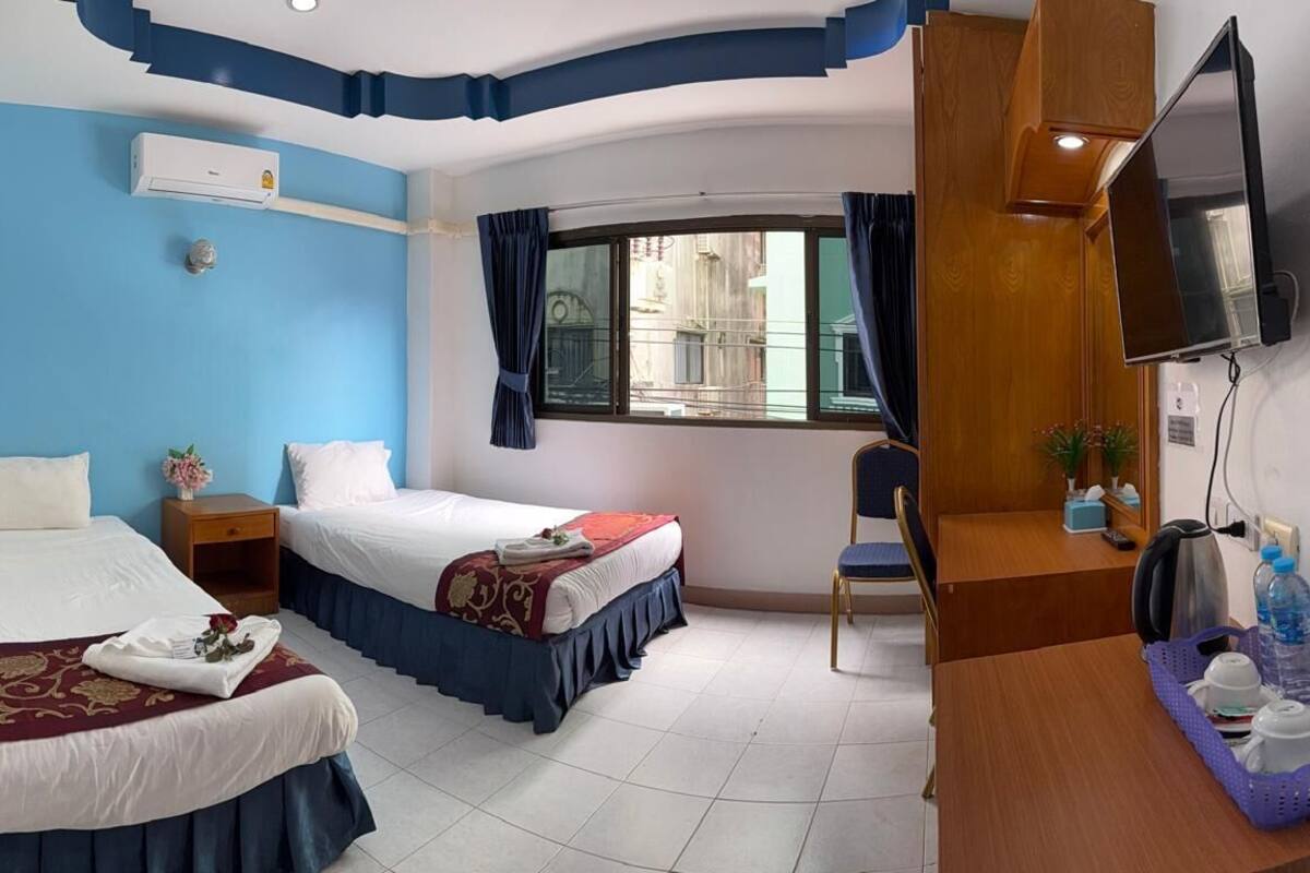 A hotel room with two beds, a desk, a TV, and a window with curtains.