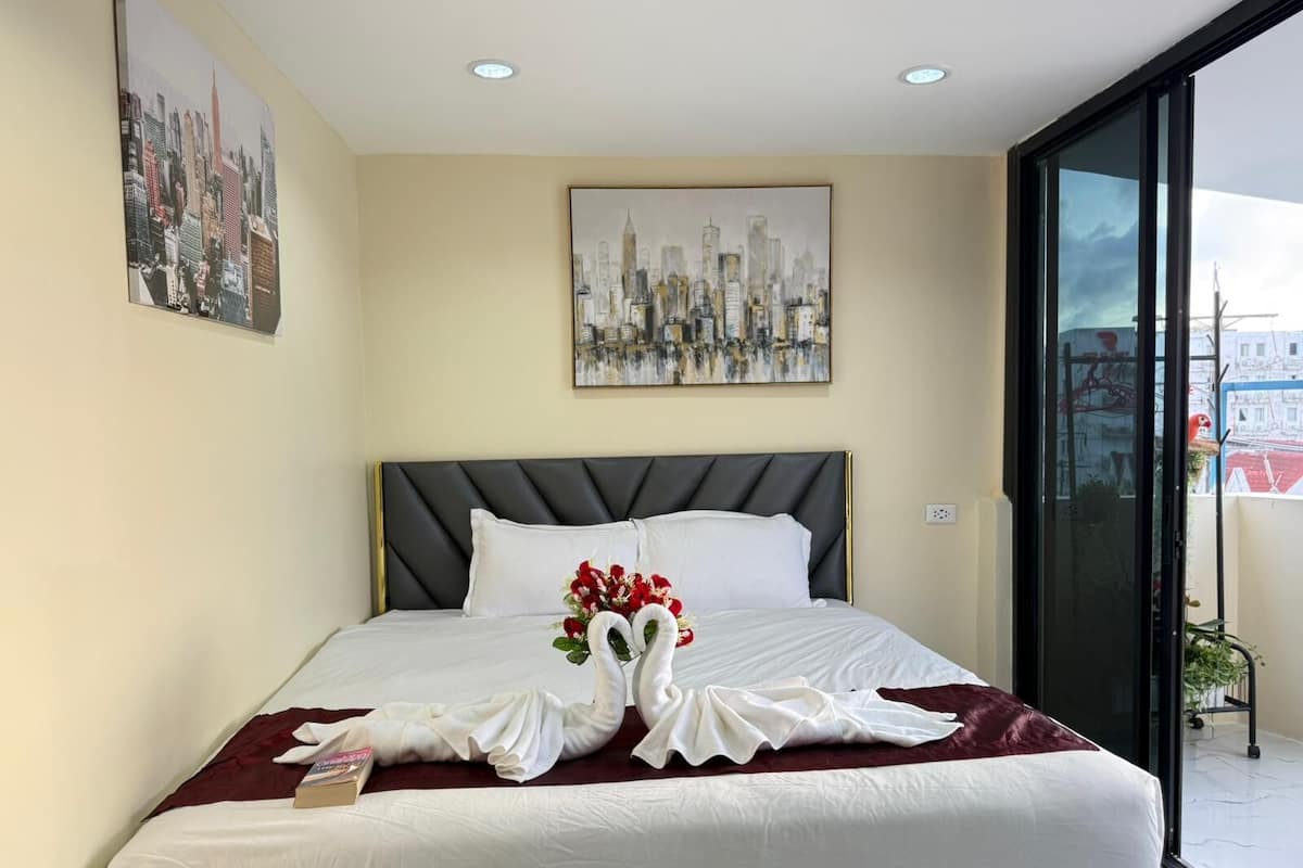 A hotel room with a bed, a cityscape painting, and a view of buildings through a glass door.