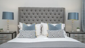 A neatly made bed with a tufted headboard, two bedside tables with lamps, and patterned pillows. - Georgian Gem in the New Town (Edinburgh)