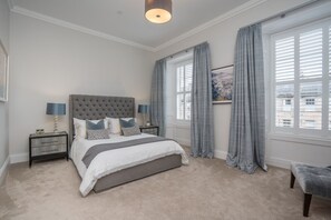 A bedroom with a tufted headboard bed, grey bedding, a bedside table with a lamp, and a window with curtains. - Georgian Gem in the New Town (Edinburgh)