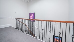 A staircase with a wooden handrail and black balusters, leading to a landing with a framed artwork. - Georgian Gem in the New Town (Edinburgh)