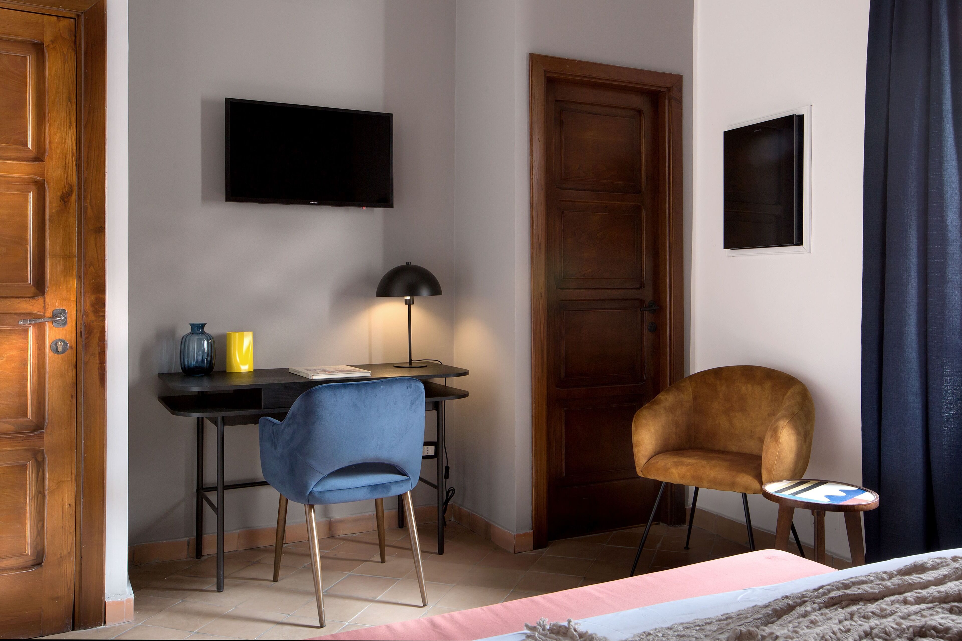 A hotel room with a bed, a desk with a chair, a television, and a door.