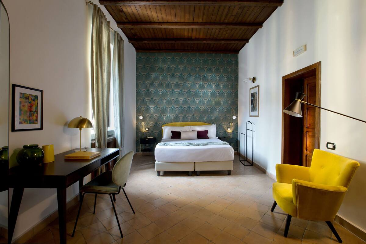 A bedroom with a bed, a desk, a chair, and a lamp.