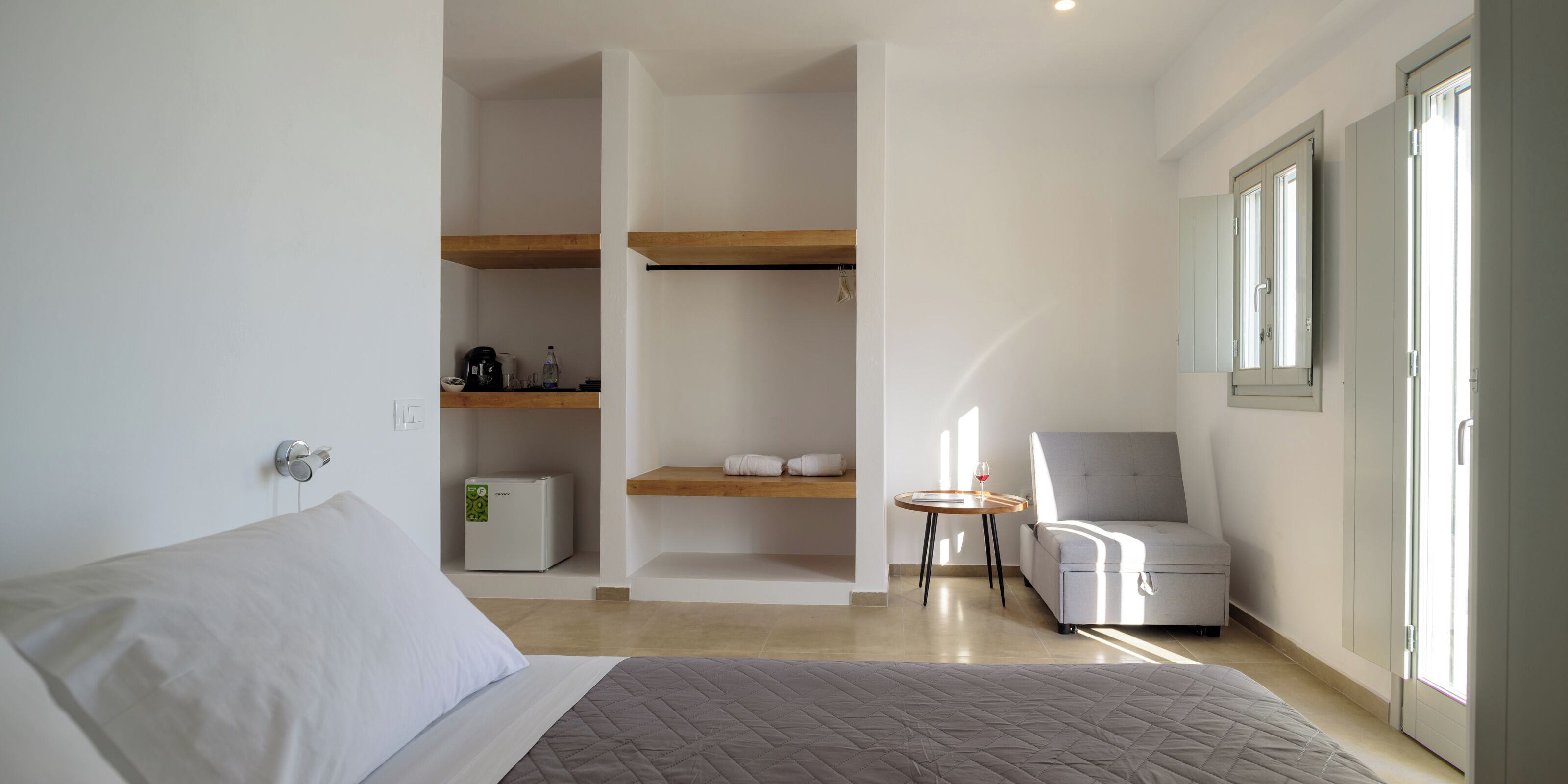 Une chambre d’hôtel moderne équipée d’un lit, d’un petit coin salon, d’un réfrigérateur et d’une fenêtre avec des stores.