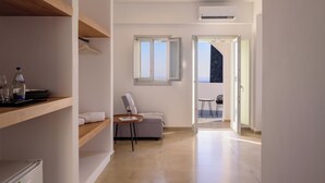 Habitación de hotel moderna con estante de madera, una mesita con una copa de vino, un sofá gris y vistas al balcón.
