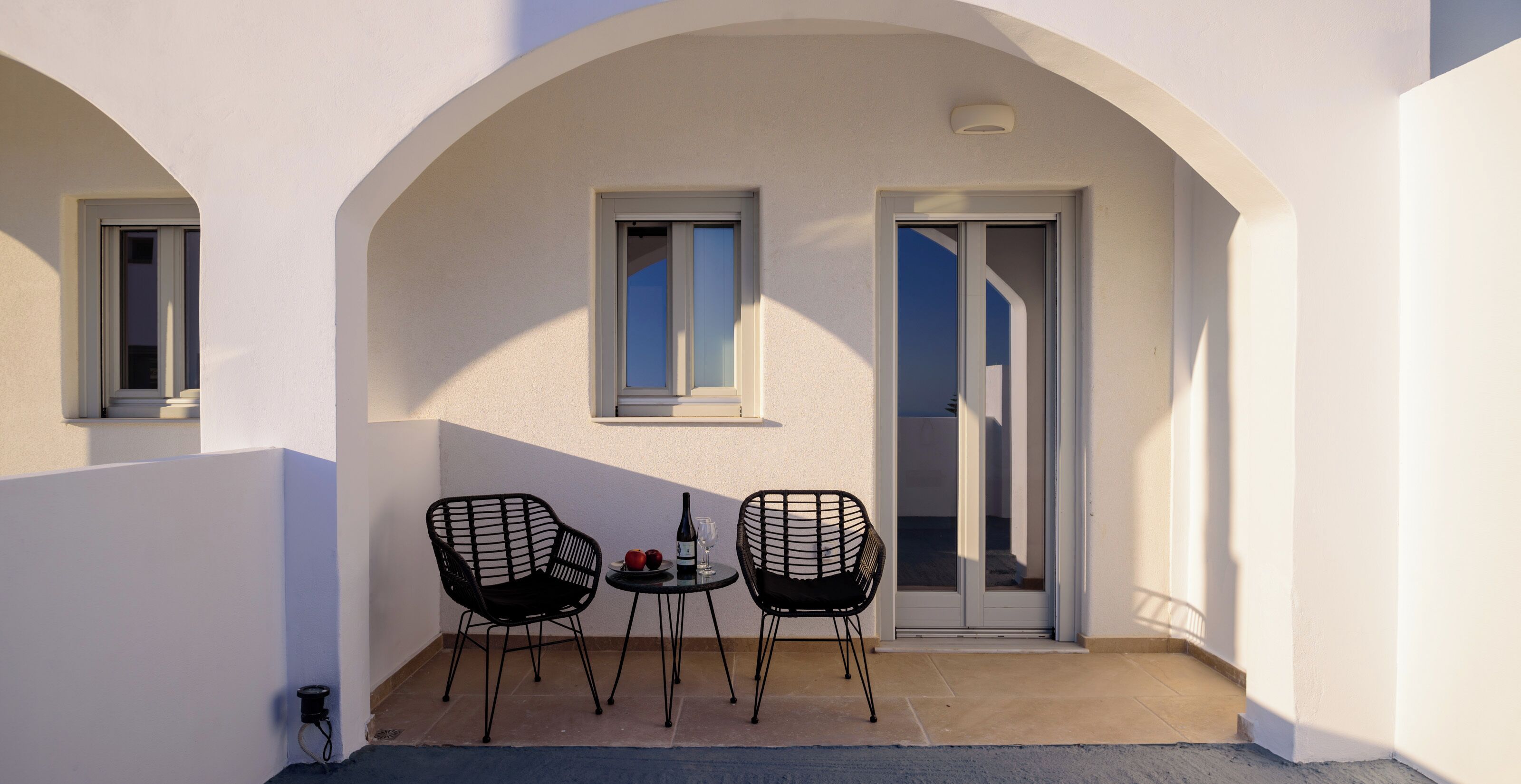 Un balcon avec deux chaises noires, une table et une bouteille de vin.