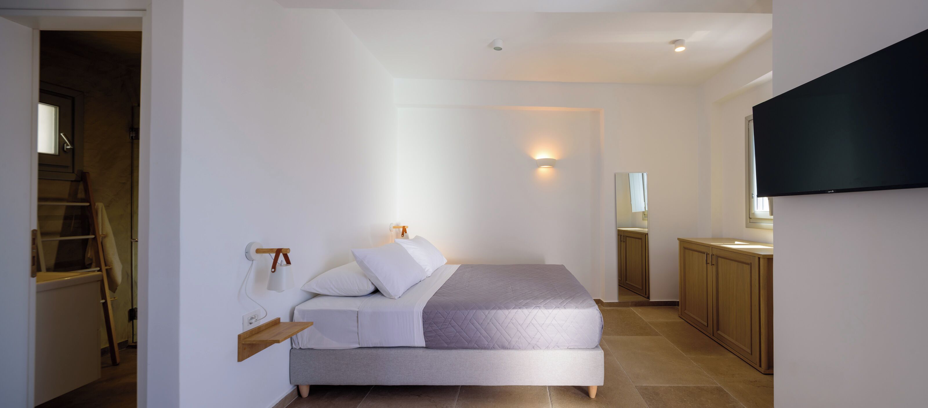Une chambre à coucher avec un lit, une table de chevet, une lampe fixée au mur et un téléviseur accroché au mur.