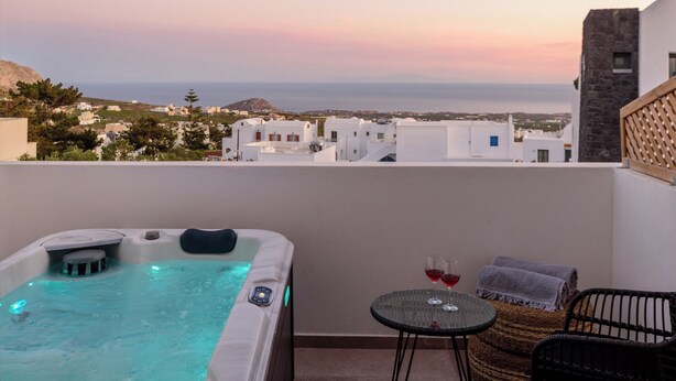 Un balcón con jacuzzi, dos copas de vino tinto y mobiliario de mimbre.