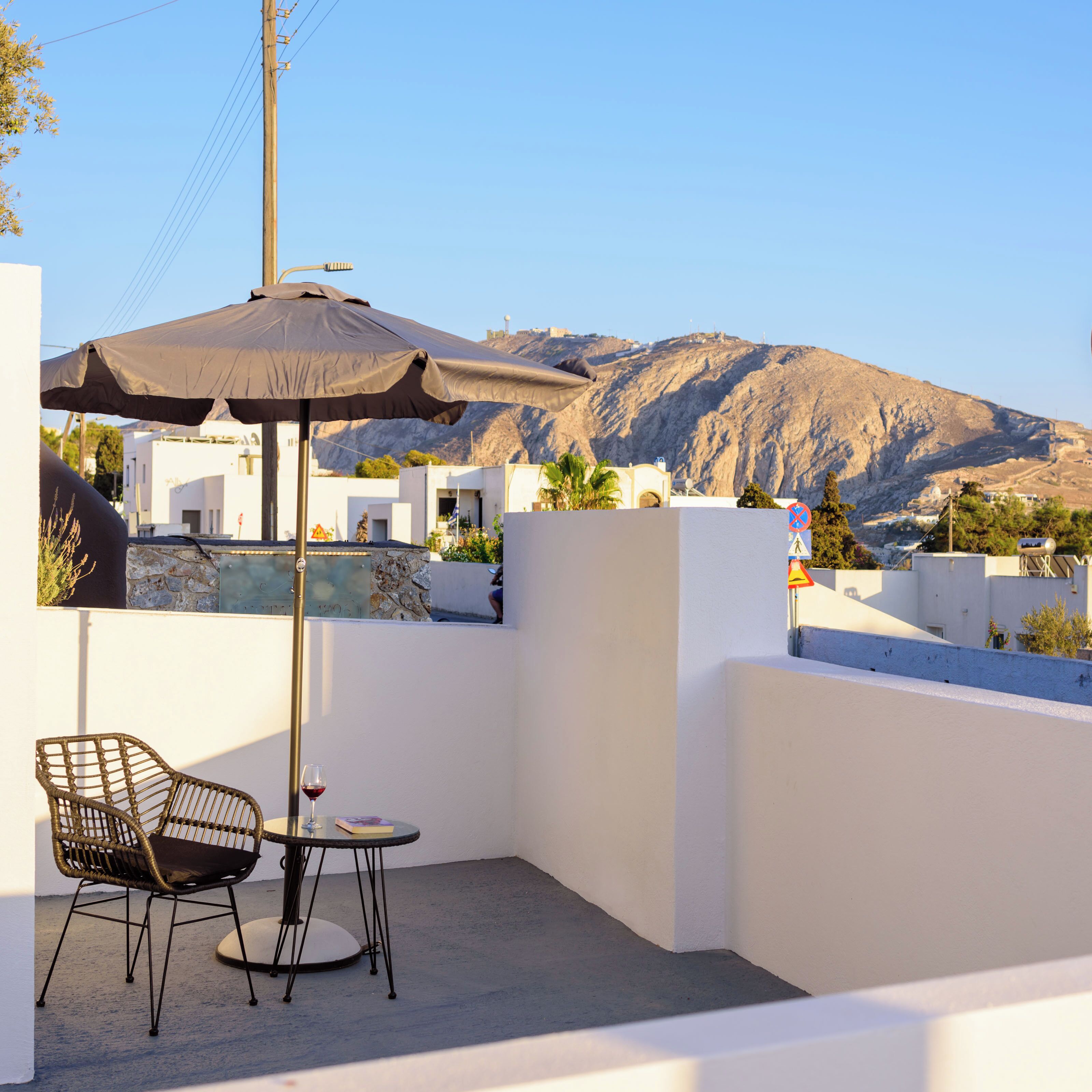 A terrace with a table and chairs, a large umbrella, and a view of a mountainous landscape.