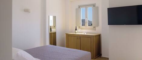 A bedroom with a bed, a wooden cabinet, a mirror, and a television on the wall.