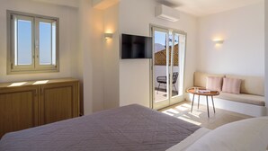 Un dormitorio con cama, televisor montado en la pared, sofá y puerta corrediza de vidrio que da a un balcón.