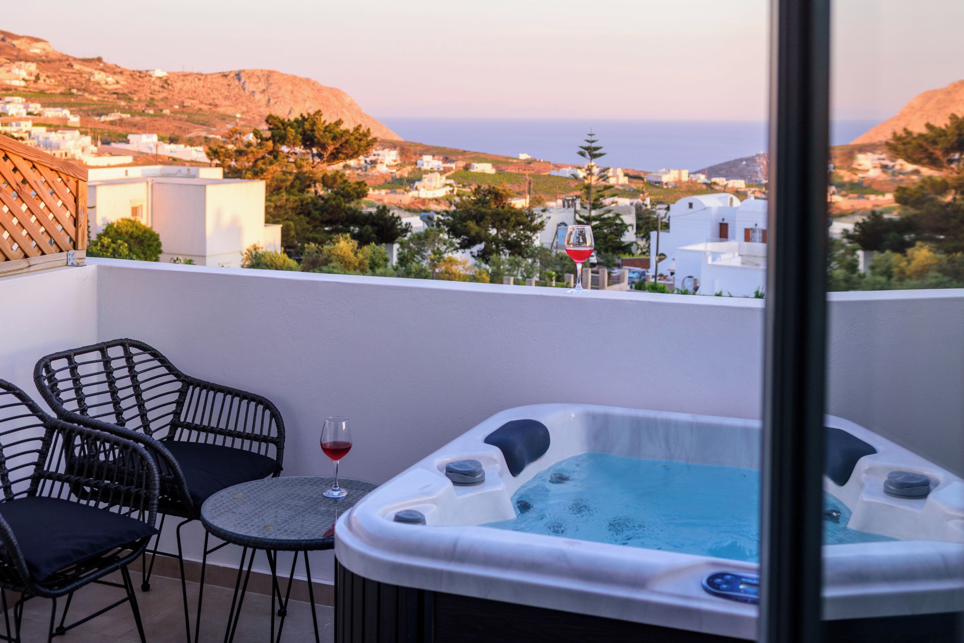A balcony with a hot tub, two wicker chairs, and a glass of red wine.