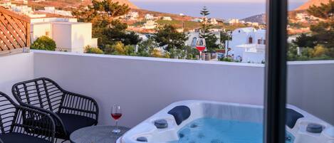 A balcony with a hot tub, two wicker chairs, and a glass of red wine.