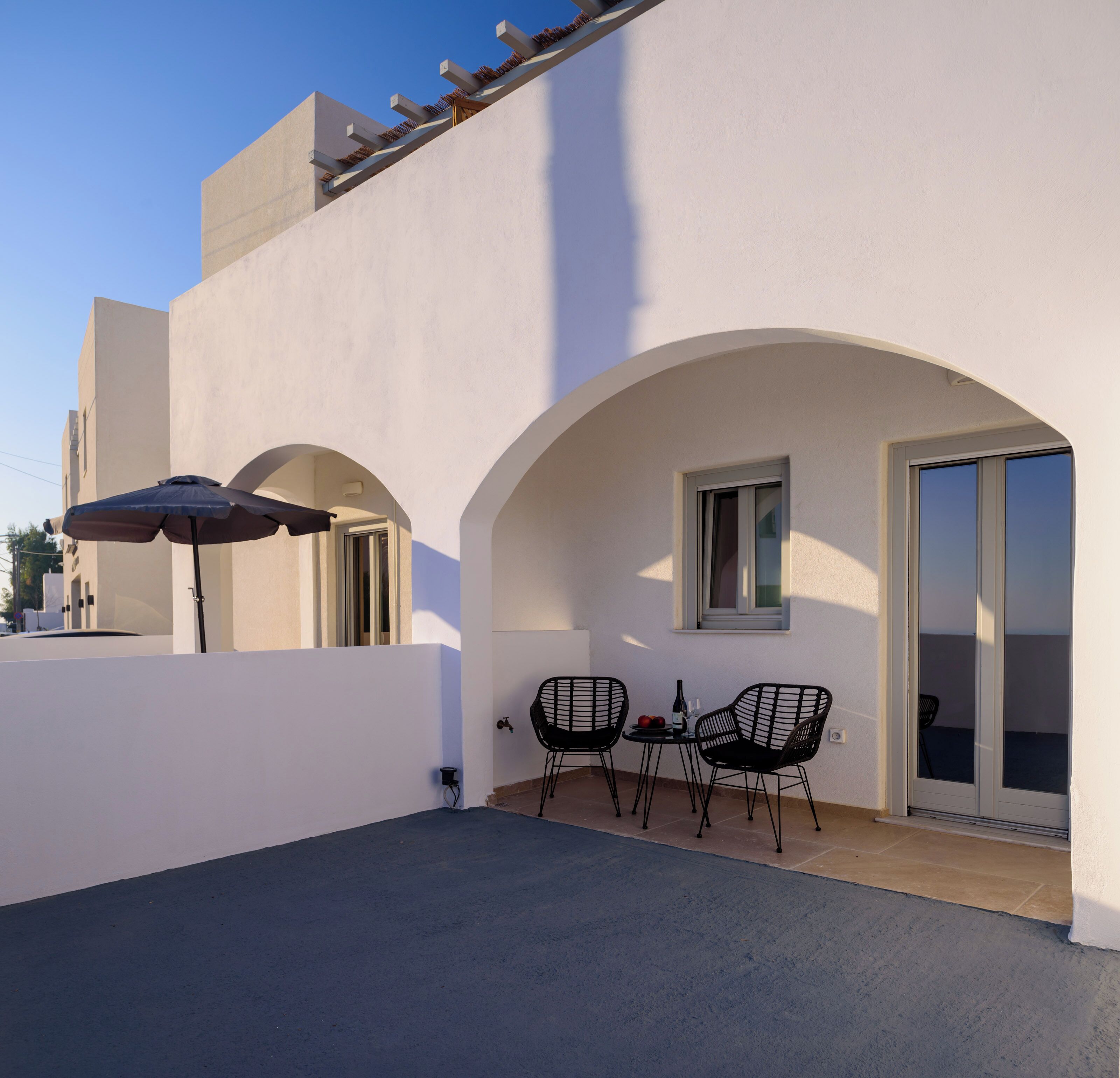 Un patio exterior moderno con dos sillas negras, una mesa y un paraguas.