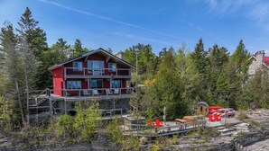 A multi-story building with a red facade and balconies, surrounded by trees and rocky terrain.