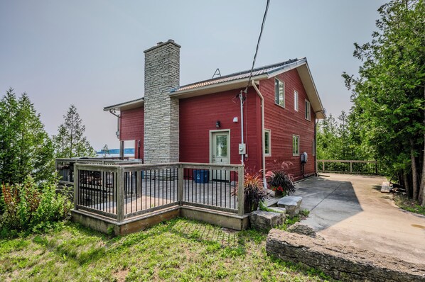 Une maison rouge avec une cheminée en pierre, une terrasse entourée d’une clôture et une allée en béton.
