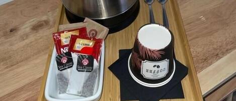 Un plateau contenant une bouilloire en acier inoxydable, deux cuillères, une théière et deux sachets de thé, posé sur une table en bois.