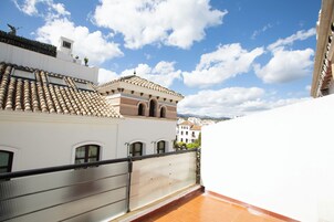 Une terrasse sur le toit, avec un toit recouvert de tuiles, une rambarde en métal et une vue sur les bâtiments environnants.