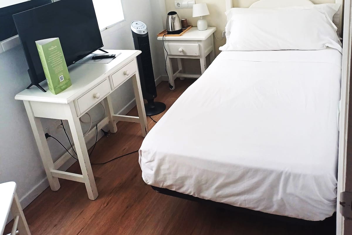 A bedroom with a bed, a desk with a computer, a lamp, and a coffee maker.