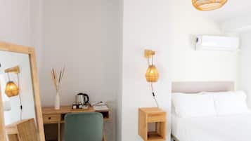 A bedroom with a bed, a desk with a chair, a mirror, and a hanging light fixture.