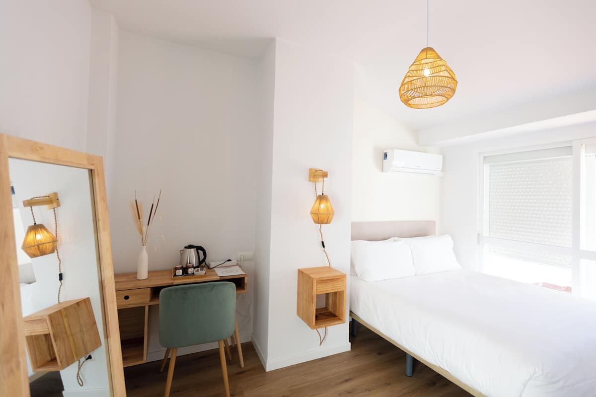 A bedroom with a wooden desk, a chair, a bed, and two hanging lamps.