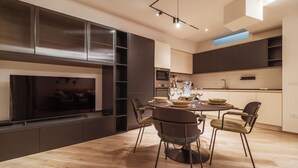 A modern kitchen with dark cabinetry, a dining area with a round table and chairs, and a built-in fireplace. - VL Luxury Apartment (Polignano a Mare)