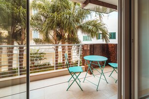 En balkon med et bord og stole, et gelænder og udsigt til palmer og bygninger.