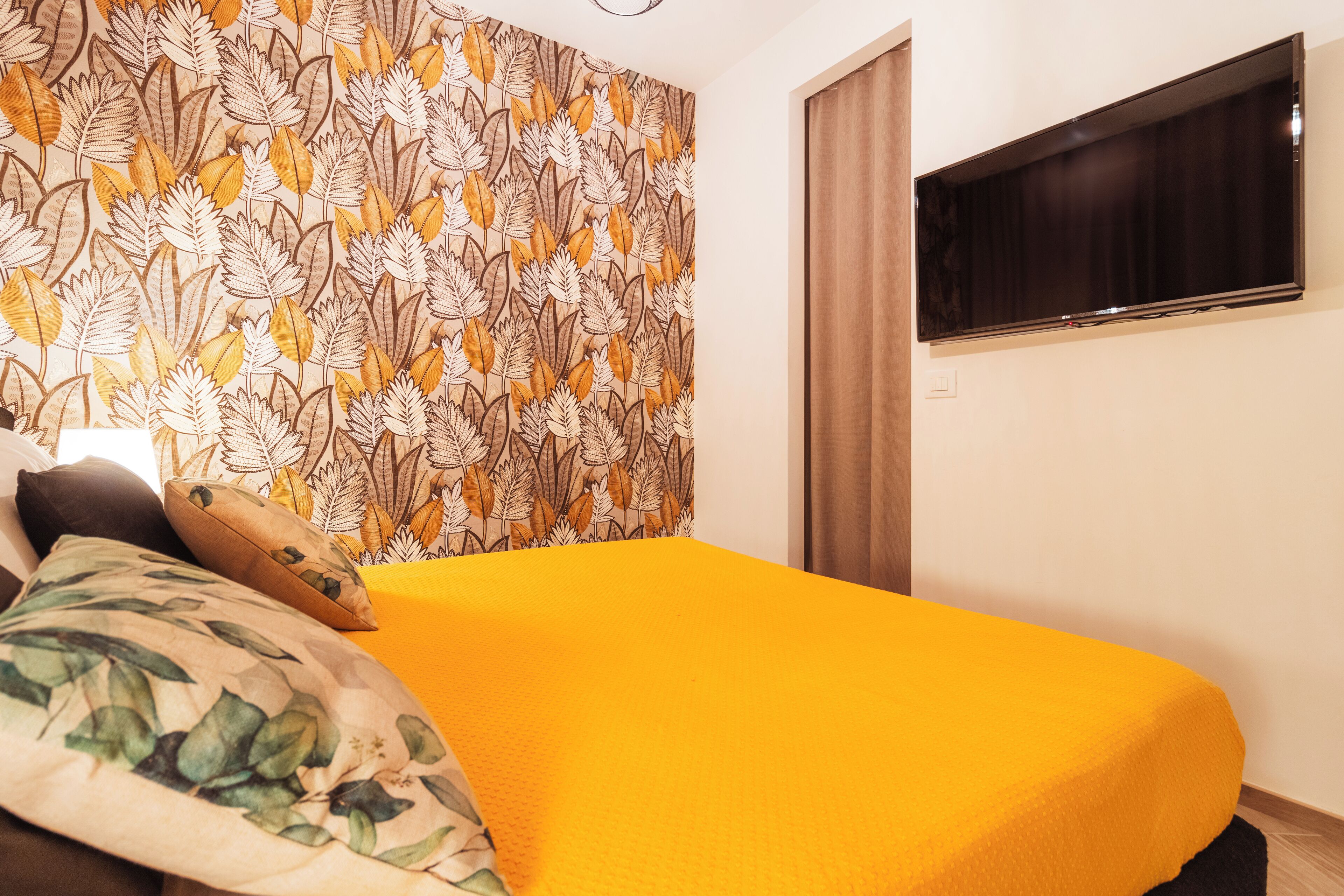 A room with a bed, a television on the wall, and a patterned wallpaper.