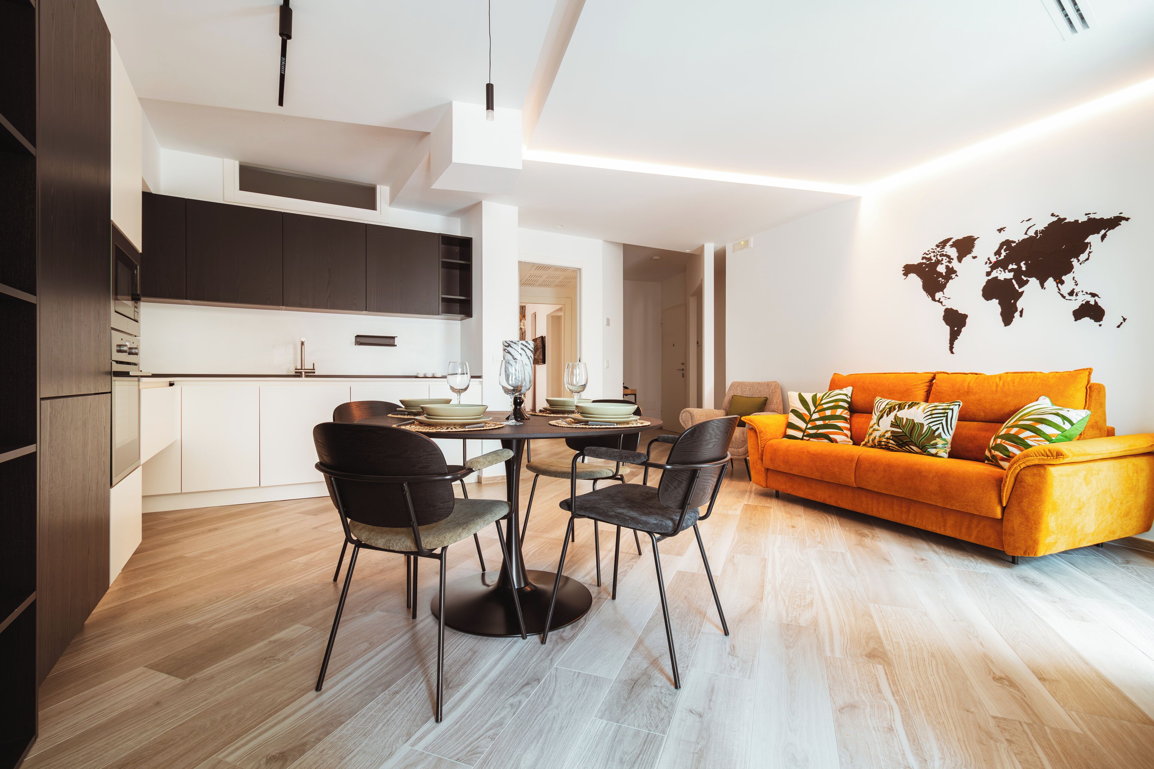 A modern living space with a dining area, kitchen, and a bright orange sofa.
