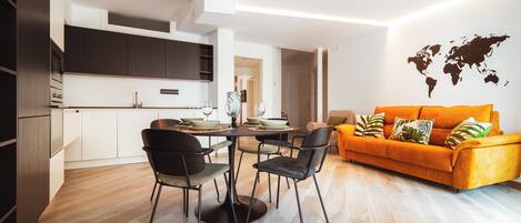 A modern living space with a dining area, kitchen, and a bright orange sofa.