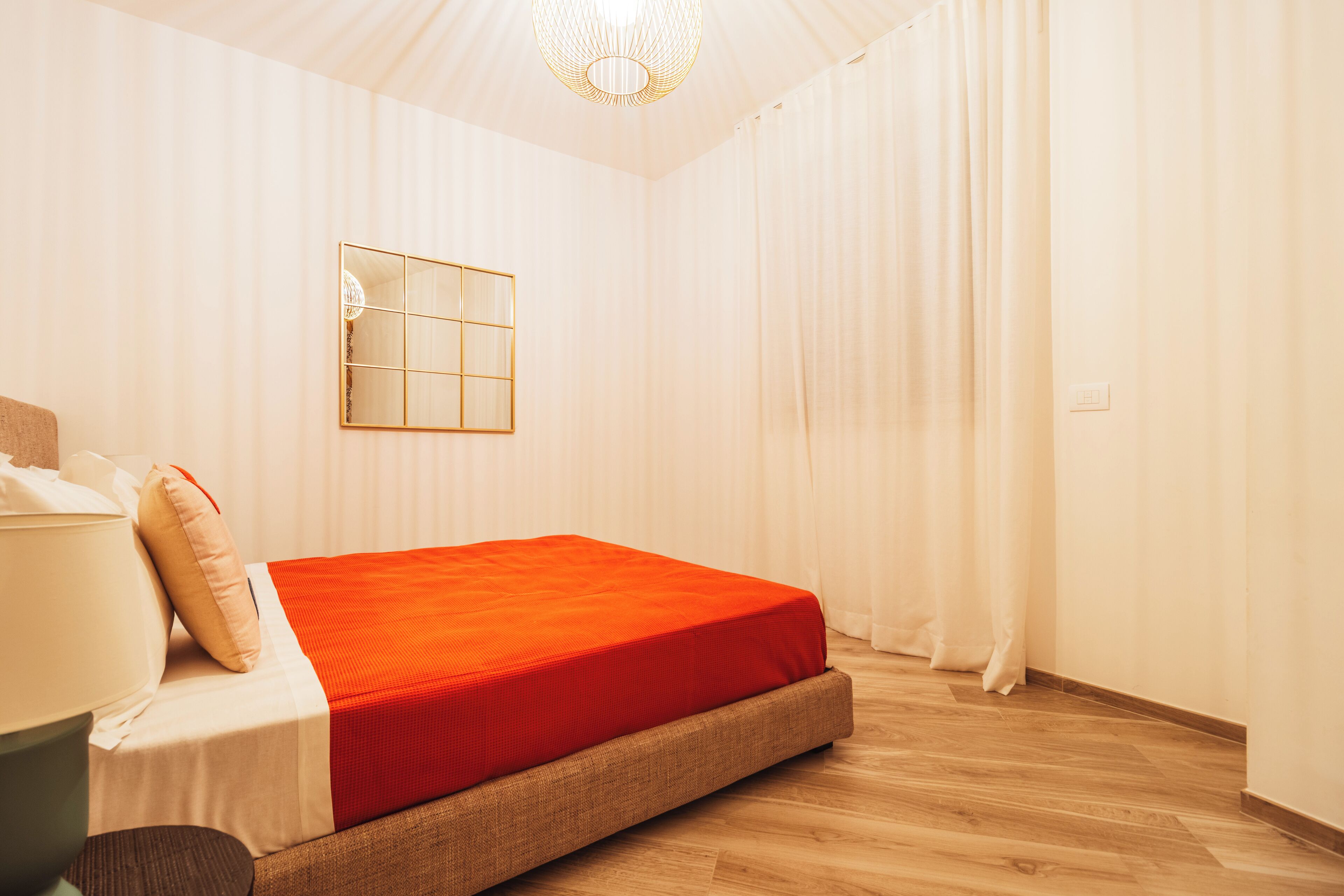 A bedroom with a bed, a bedside table, a lamp, and a mirror on the wall.