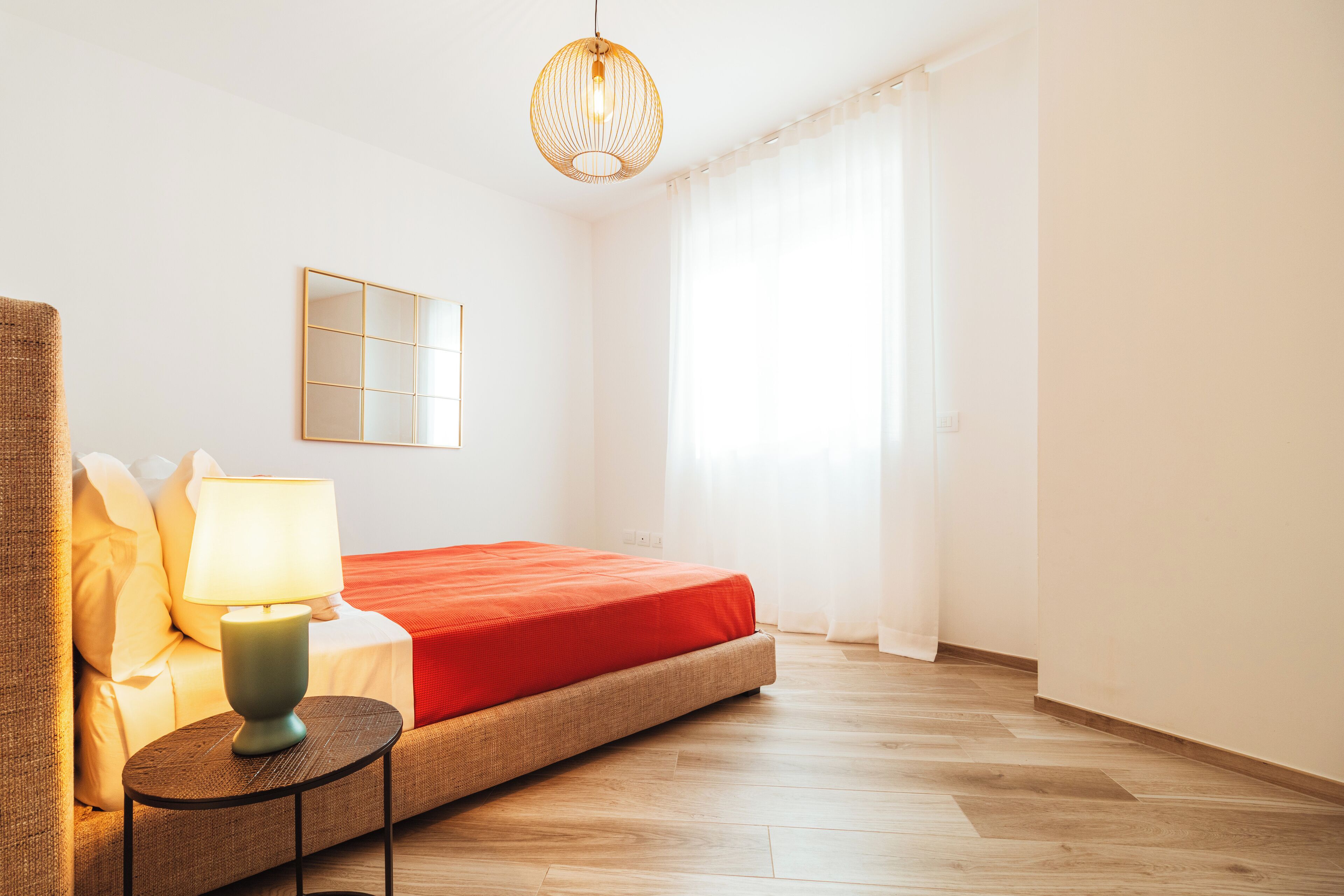 Une chambre à coucher avec un lit, une table de chevet avec une lampe, un miroir et une fenêtre avec des rideaux.