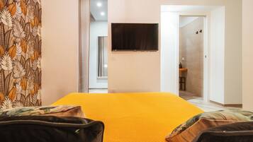 Quarto de hotel com uma cama grande, televisão de tela plana na parede e banheiro visível por uma porta aberta.