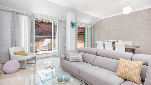 Un salon moderne avec un canapé gris, une table basse en verre et un coin repas comprenant des chaises blanches et une table en bois.