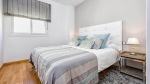Une chambre avec un grand lit, une table de chevet, une lampe et une fenêtre avec des stores.