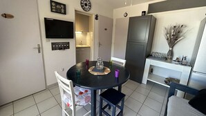Une cuisine compacte comprenant une table à manger, des chaises, un réfrigérateur et un téléviseur fixé au mur.