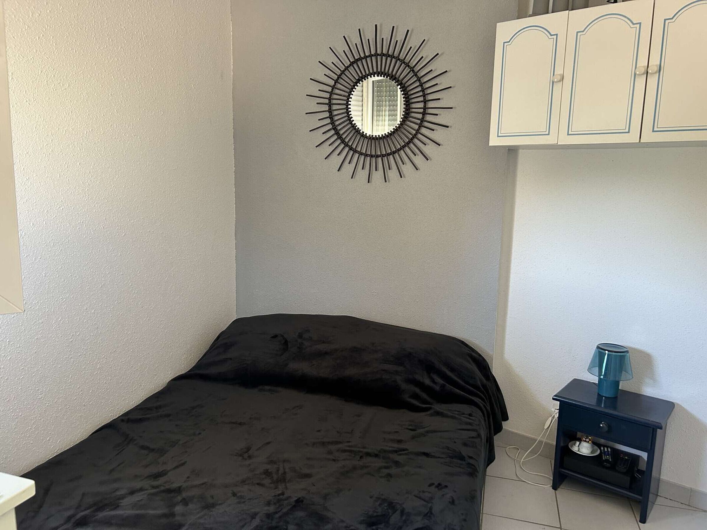 Une chambre à coucher comprenant un lit, un miroir fixé au mur, une table de chevet avec une lampe et une armoire.