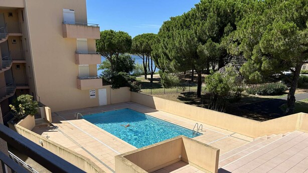 Une piscine à l’eau d’un bleu limpide, entourée d’une terrasse carrelée de couleur beige et d’un petit muret.
