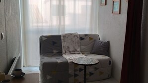 A living room with a sofa, a small round table, and a window with sheer curtains. - Cozy 1BR Apt for 4, Near Beach, Parking, WiFi, Pet-Friendly (Argelès-sur-Mer)