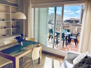 Una sala de estar moderna con una mesa de comedor de vidrio, un sofá y un balcón con mobiliario de exterior.