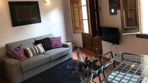 Un salon avec un canapé gris, une table basse en verre et une porte en bois.