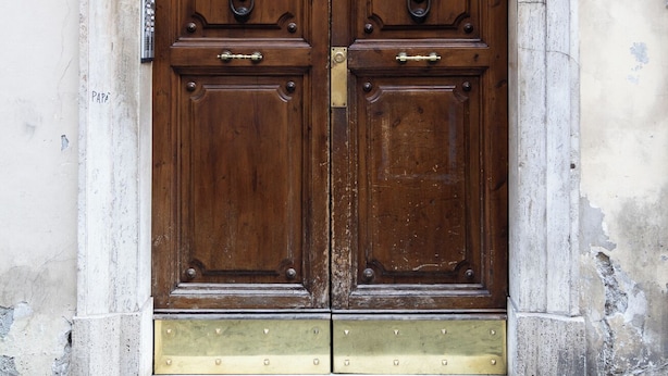 A double wooden door with a brass threshold and lion head knockers, set in a stone archway. - Boccaccio 22 - 4 (Roma)
