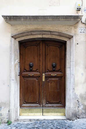 A double wooden door with a brass threshold and lion head knockers, set in a stone archway. - Boccaccio 22 - 4 (Roma)